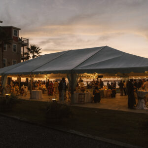 Beachfront party venue with white tent and guests at sunset - Regatta Inn